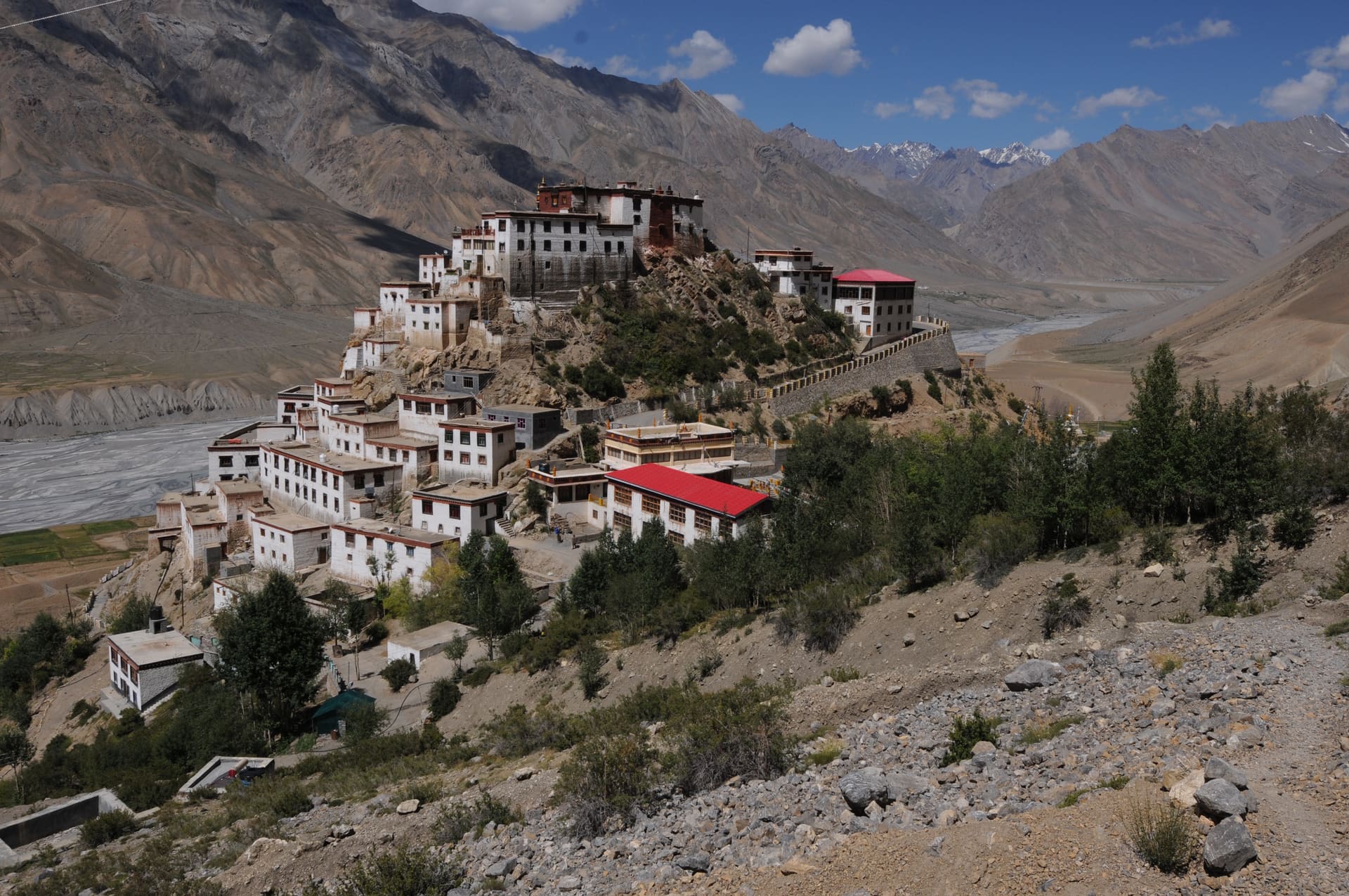 Key Monastery, white buildings with red roofs on a rocky spur above a wide valley, with bare mountains and a few snowy peaks behind.