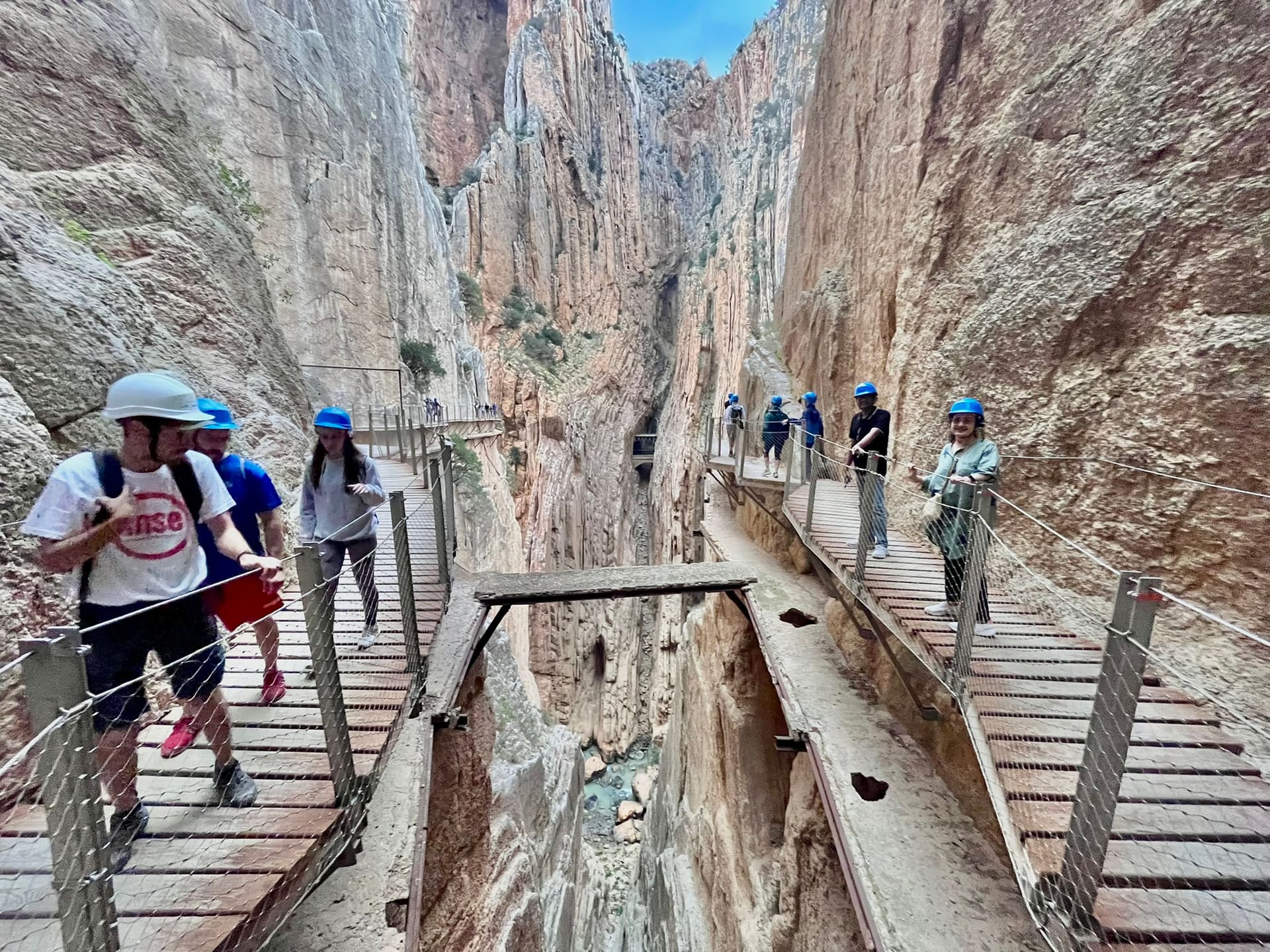 People in helmets walk on wooden boardwalks fixed to both walls of a deep gorge, with the drop between the paths.